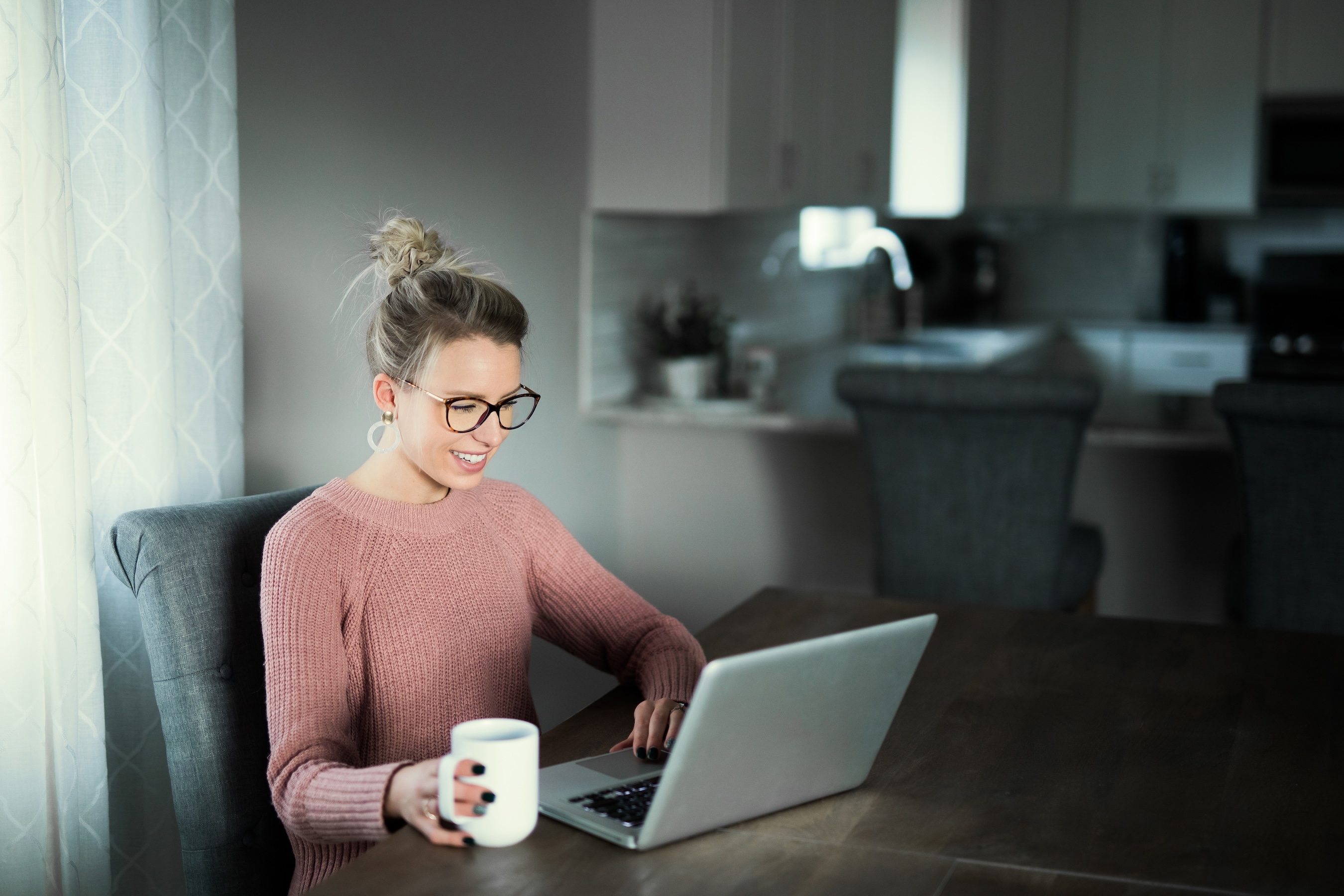 A woman sat at her desk on a laptop with a coffee
